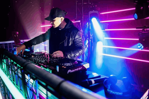 DJ mixing on Pioneer CDJs with blue and pink beam lighting behind