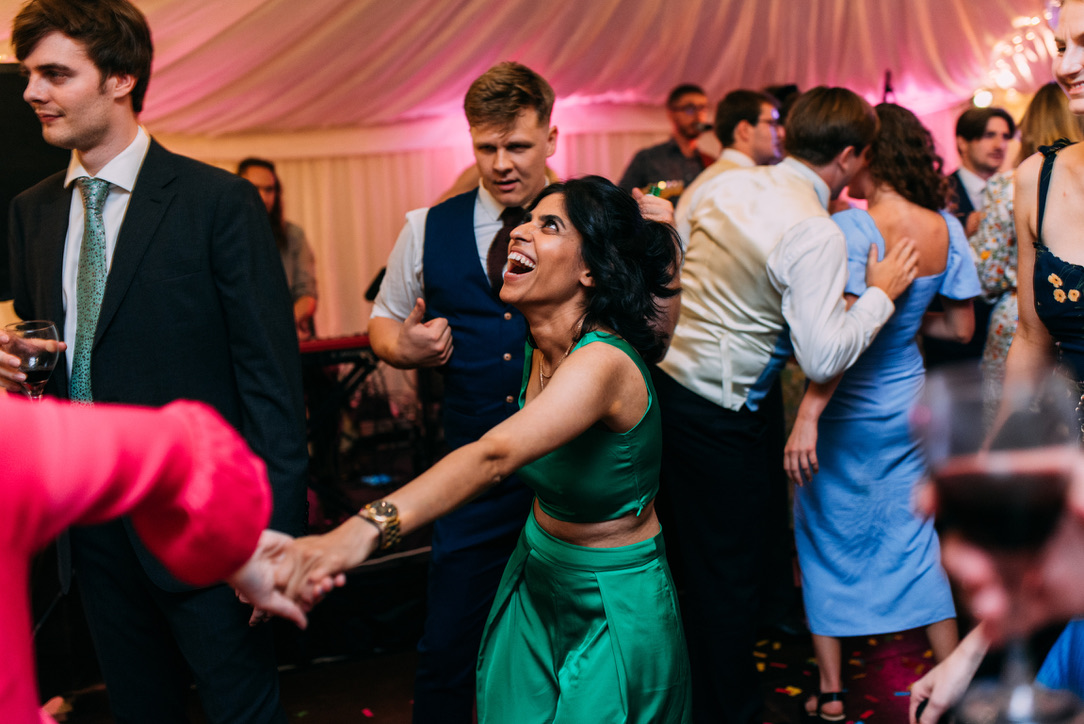 Wedding guests dancing and laughing under pink uplighting in a marquee