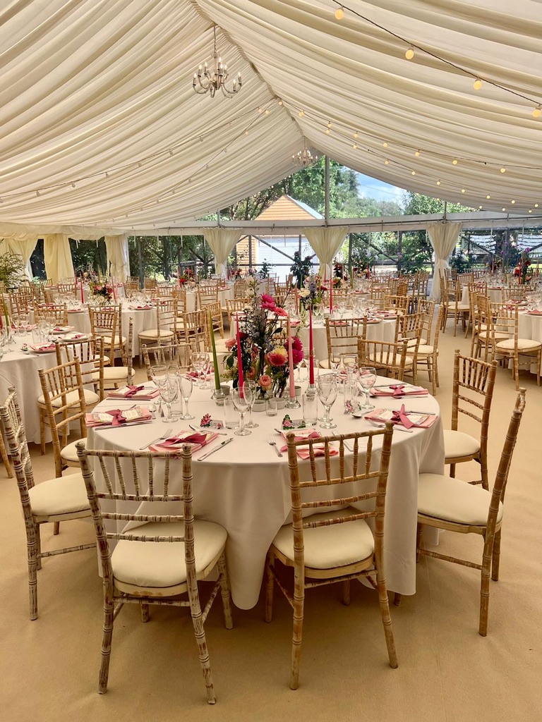 Round tables dressed in white linen with pink napkins, tapered candles and seasonal flowers under a lined marquee