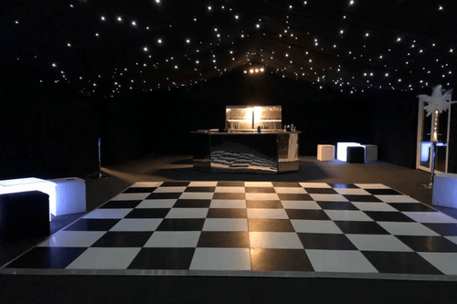 Black and white checkered dancefloor inside the marquee with illuminated cube seating and the mirrored bar behind