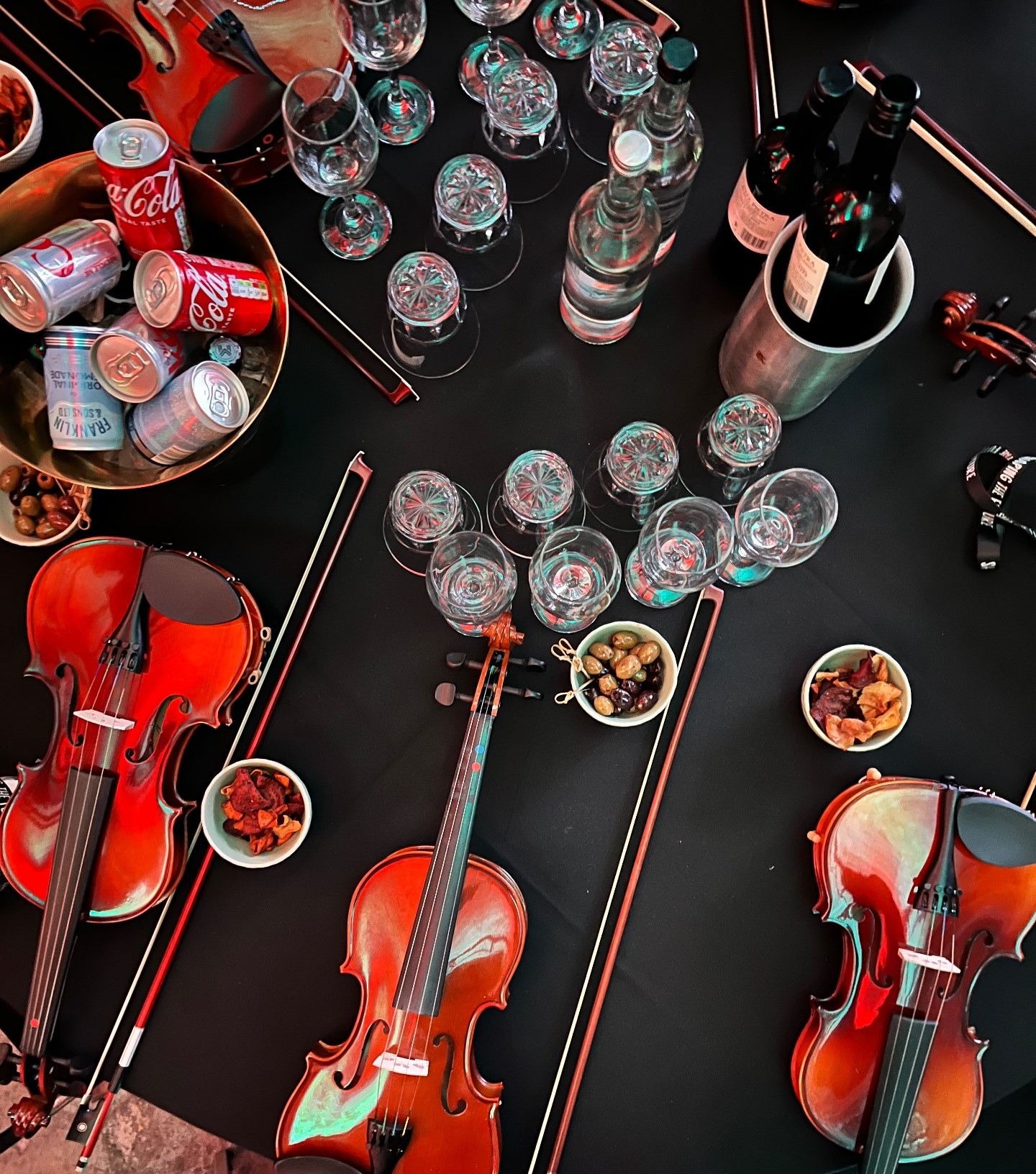 Overhead view of a black-linen table dressed with violins, bows, wine glasses and canapés ready for a musical performance