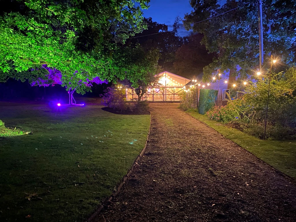 Festoon-lit garden path leading to a marquee at dusk