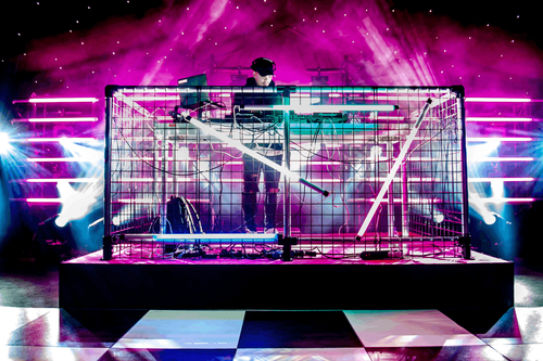 Caged DJ staging structure lit in magenta with neon strip lighting and stage haze
