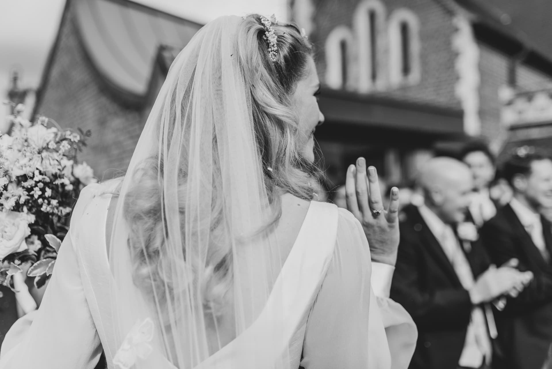 Black and white photograph of a bride in a veil greeting guests outside the church after the ceremony