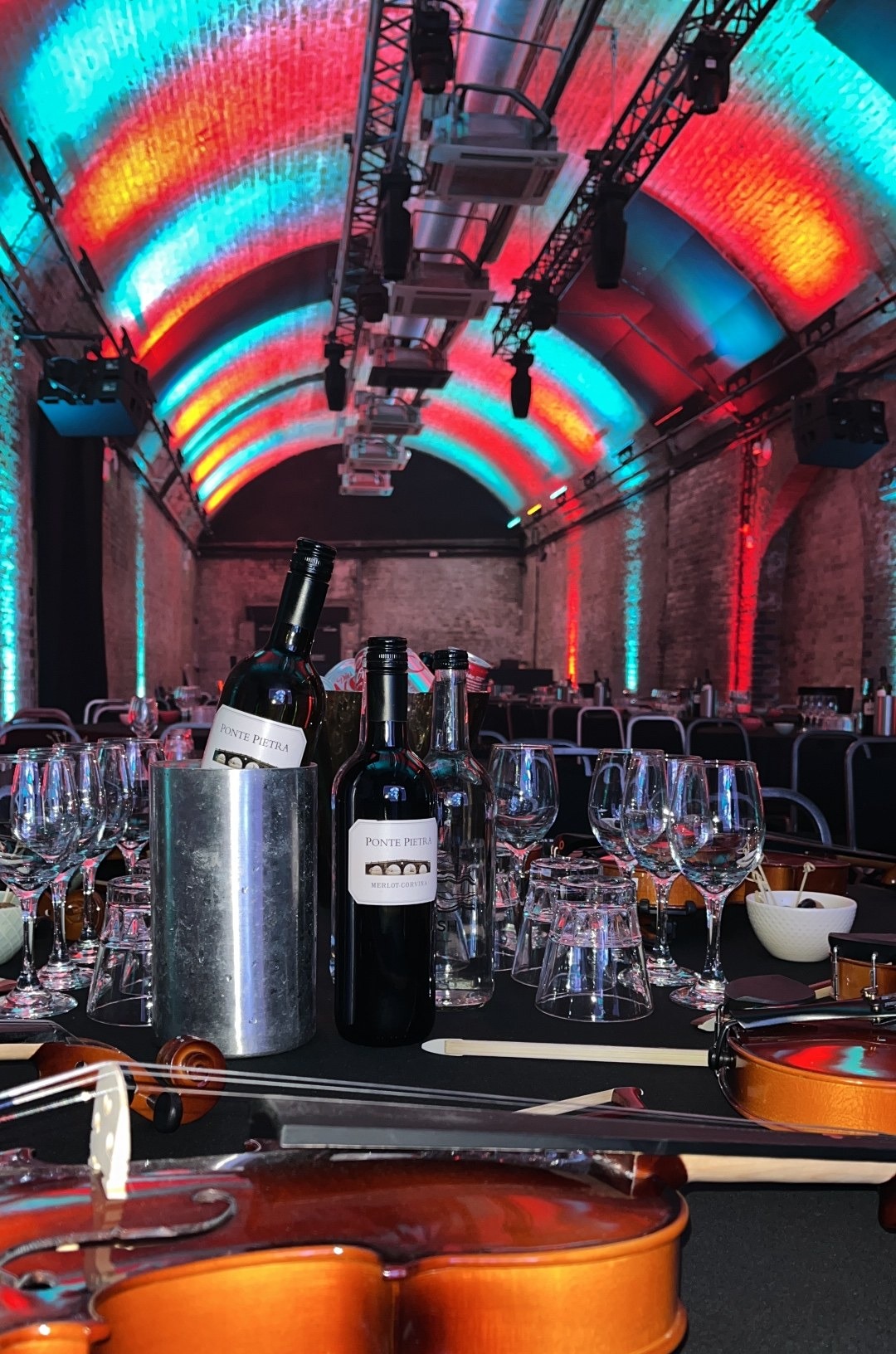 Long banqueting tables laid up in a brick tunnel venue with dramatic red and teal ceiling lighting